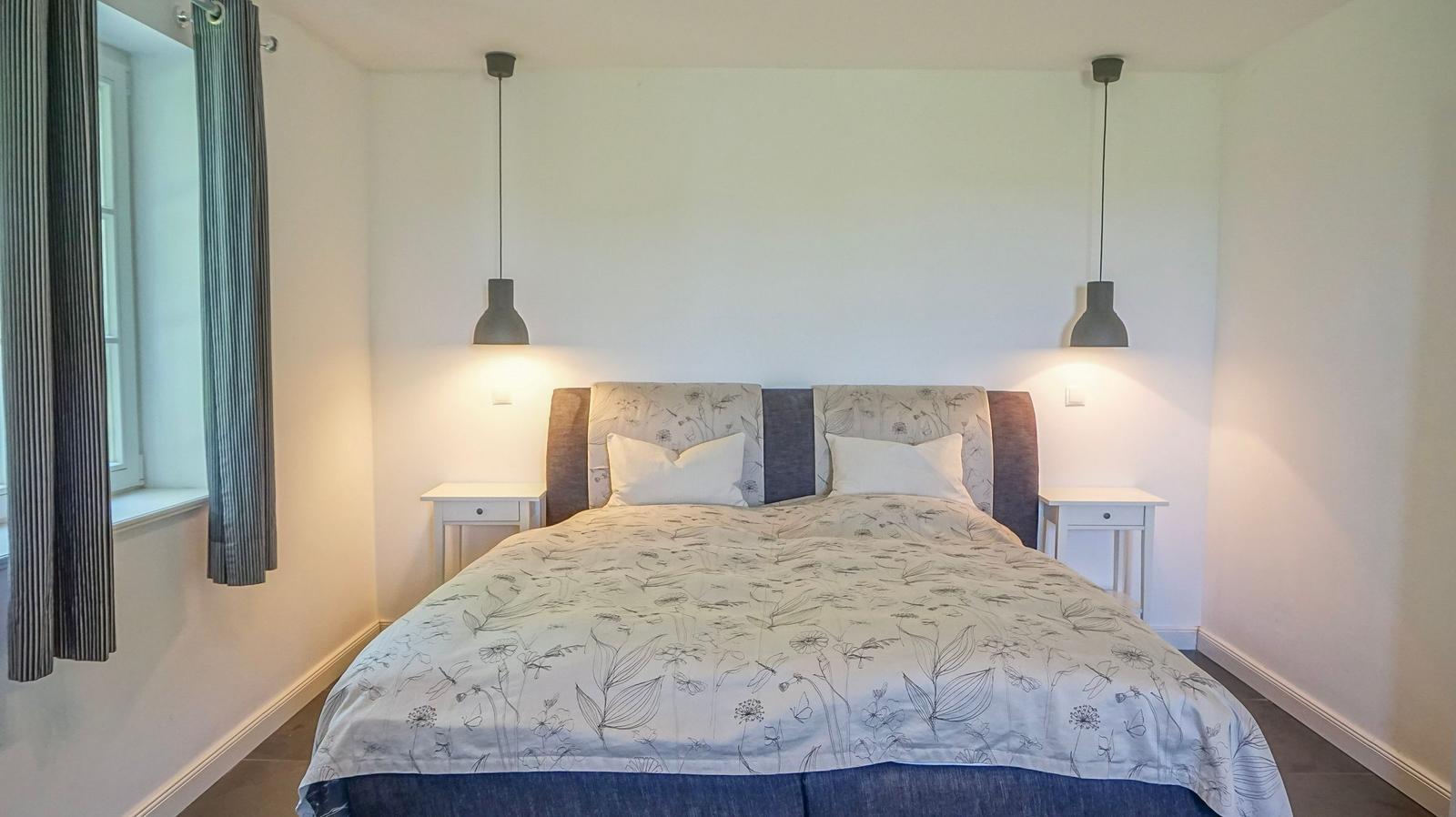 Schlafzimmer mit Bett, zwei Nachttischen und hängenden Lampen.