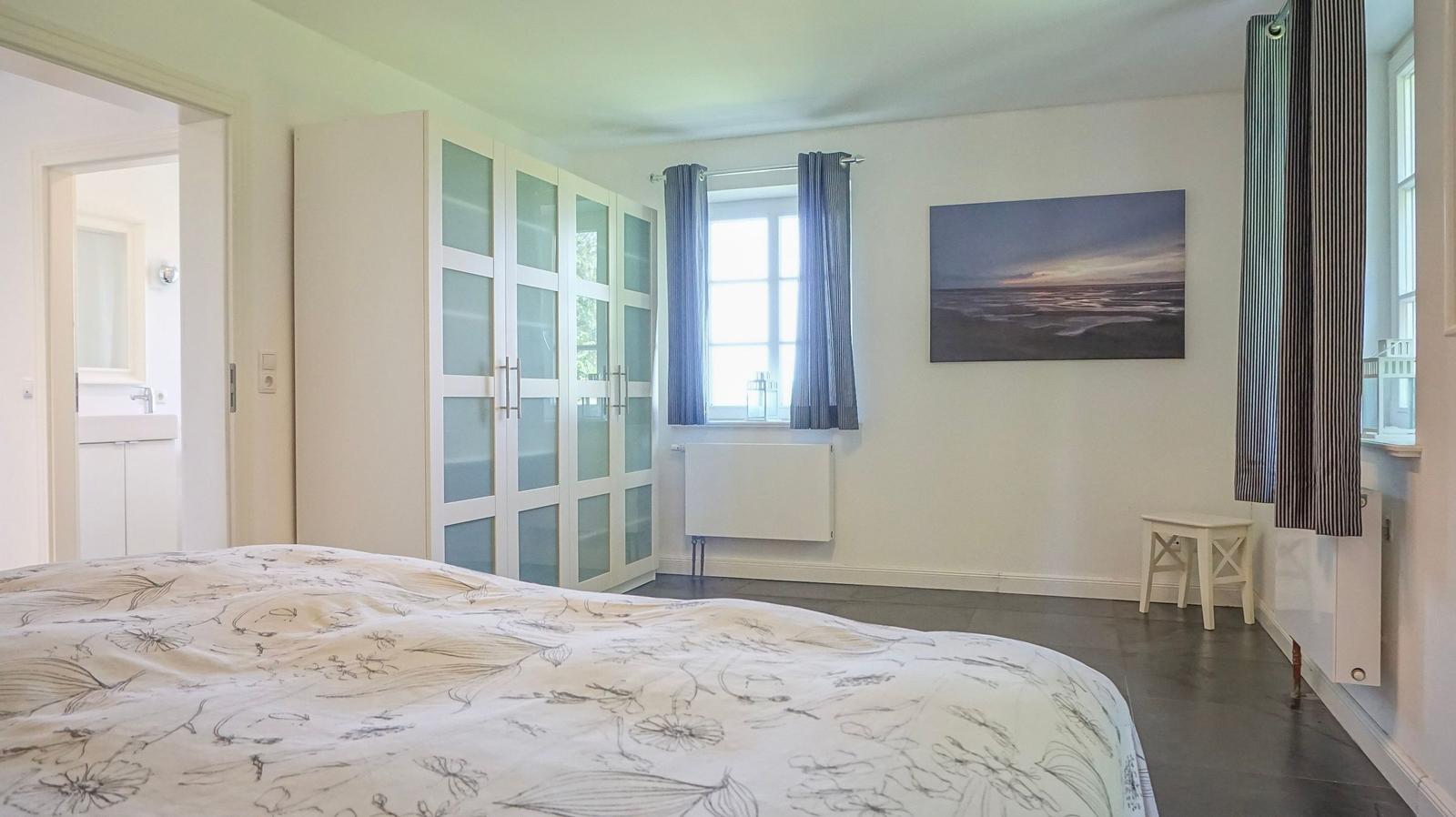 Schlafzimmer mit Bett, Kleiderschrank, Fenster und Wandbild.