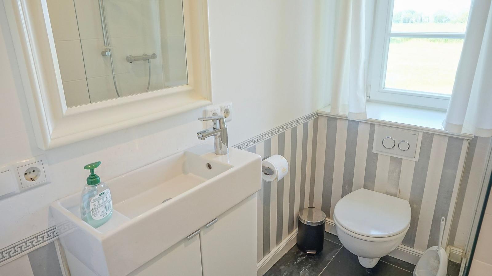 Badezimmer mit Waschbecken, Toilette und Dusche. Wandverkleidung mit Streifenmuster.