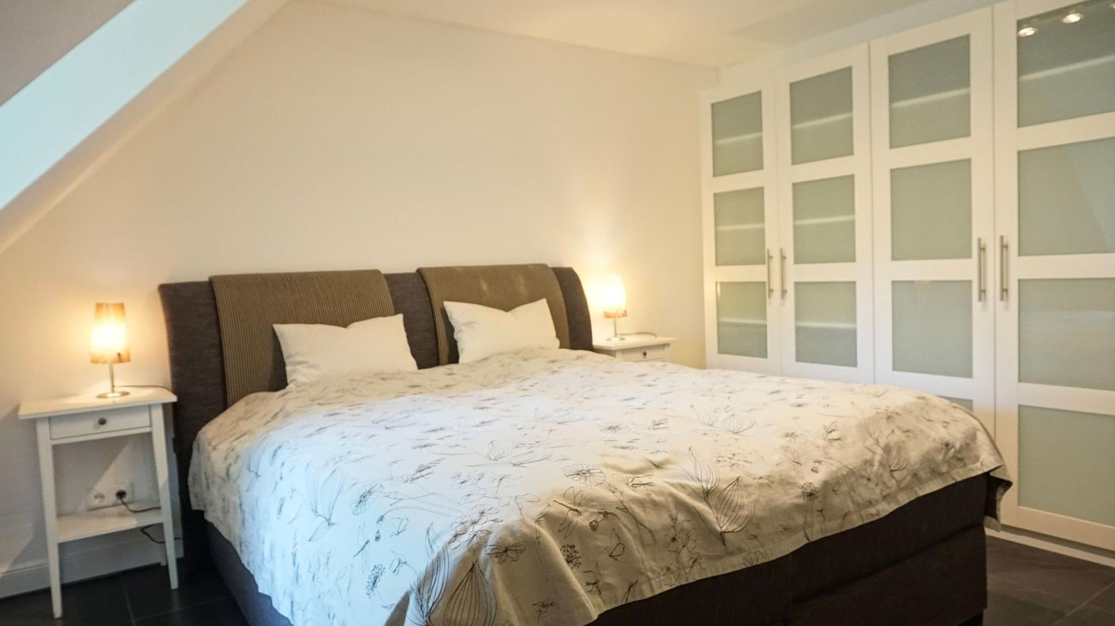 Schlafzimmer mit Doppelbett, Nachttischen und Schrank unter Dachschrägen.