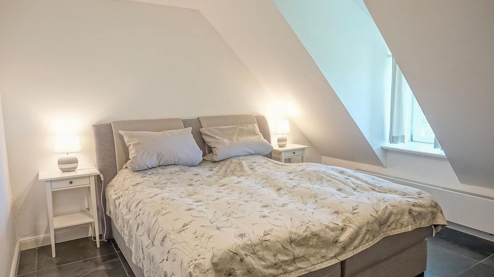 Schlafzimmer mit Doppelbett, zwei Nachttischen und einem Dachfenster.