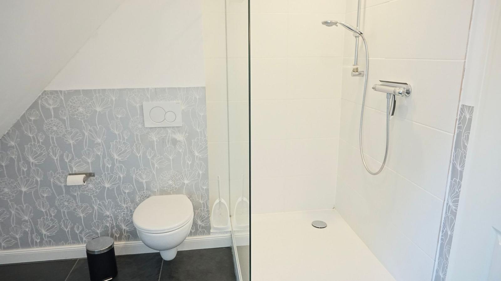 Bad mit Dusche und WC, Wand mit floraler Tapete, bodenfliesen und Glaswand