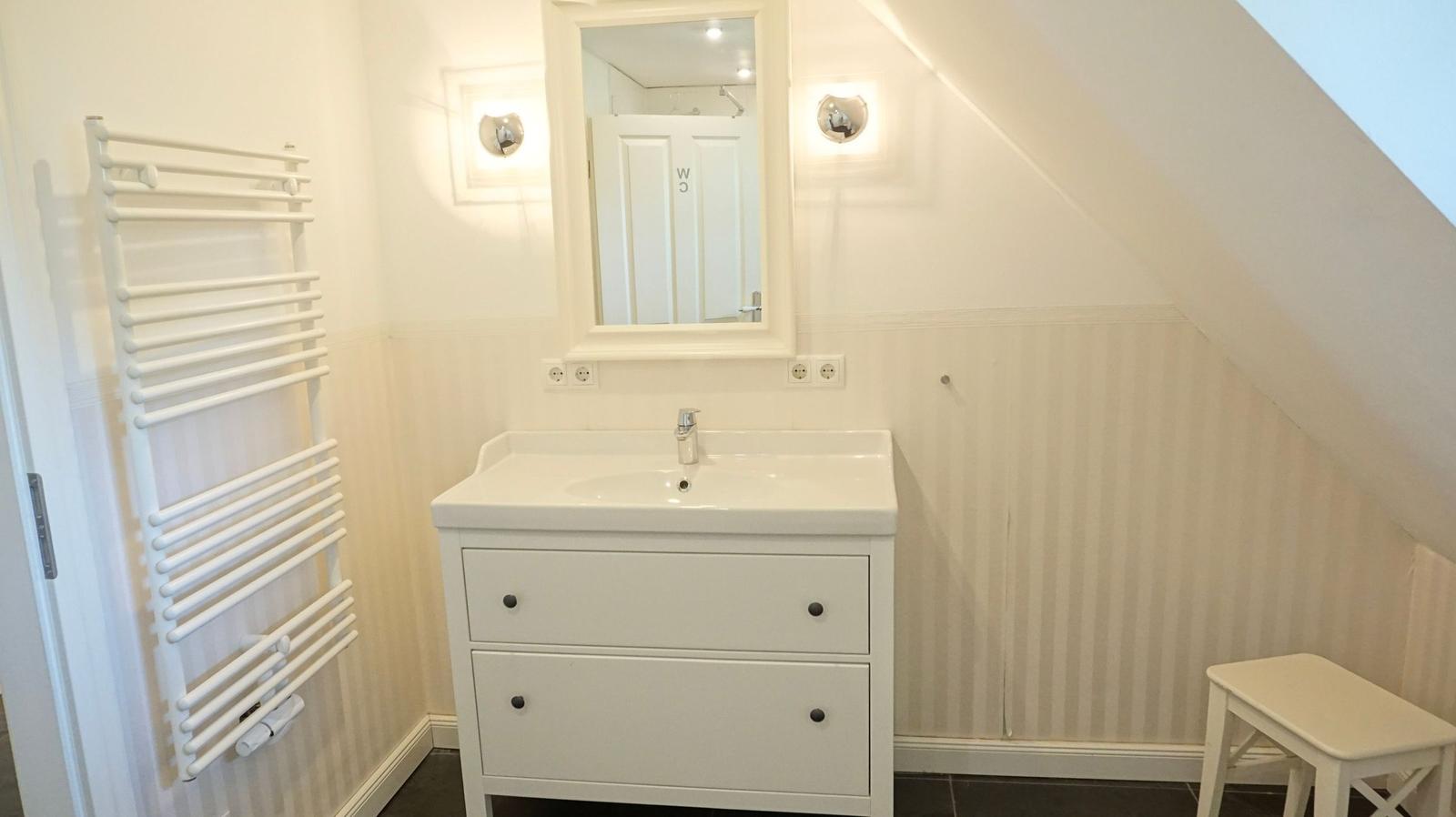 Badezimmer mit Waschbecken, Spiegel, Heizung und Stuhl unter Dachschräge.