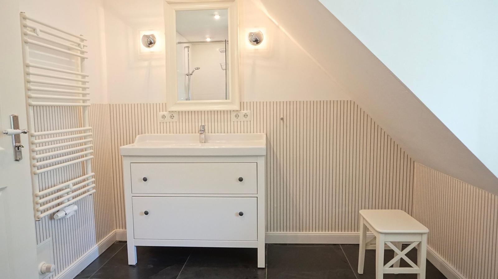 Badezimmer mit Waschbecken, Spiegel, Dusche und Heizkörper