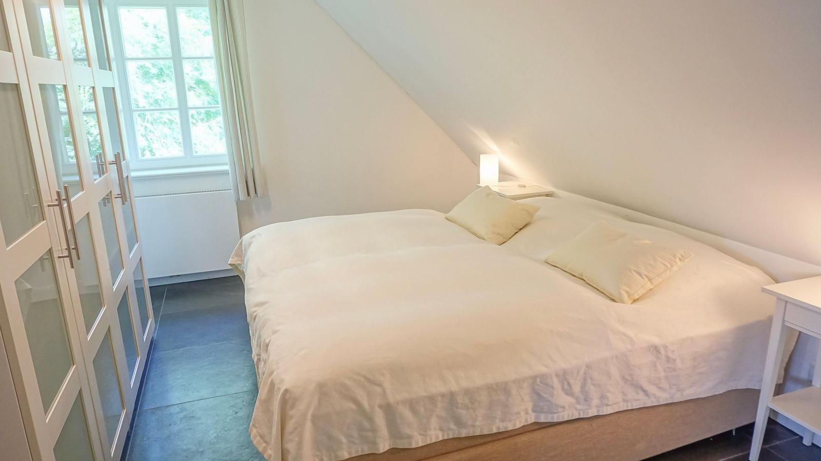 Schlafzimmer mit Doppelbett, Fenster und Kleiderschrank.