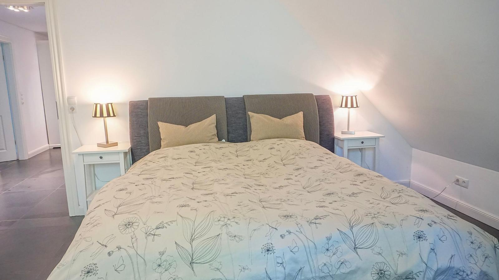 Schlafzimmer mit Doppelbett, zwei Nachttischen und Lampen an den Seiten.