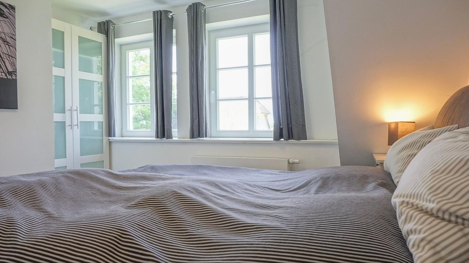 Schlafzimmer mit Bett, Fenstern und Gardinen.