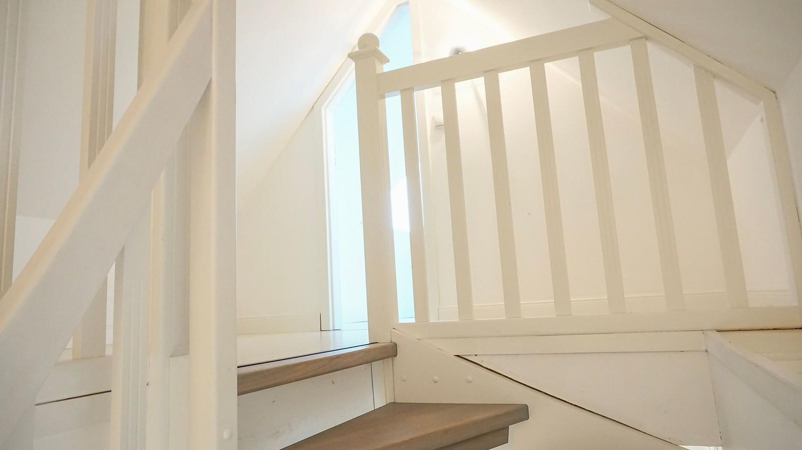 Treppenhaus mit weißer Holzgeländer und Holzstufen in einem hellen Raum.