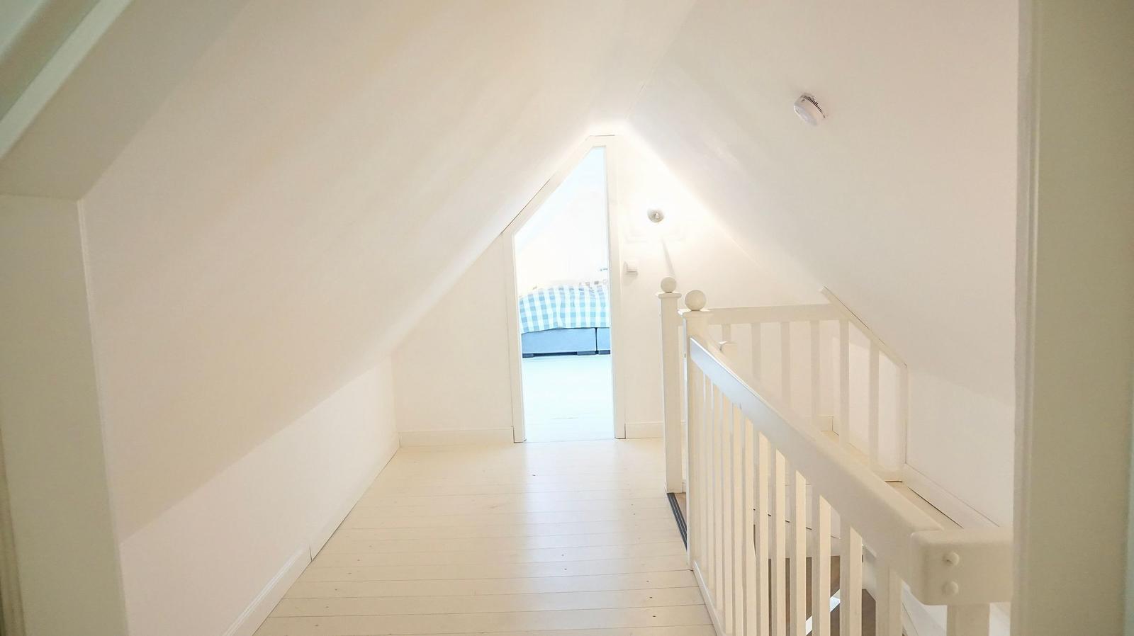 Flur mit weißer Treppe und Blick in Schlafzimmer mit Bett.