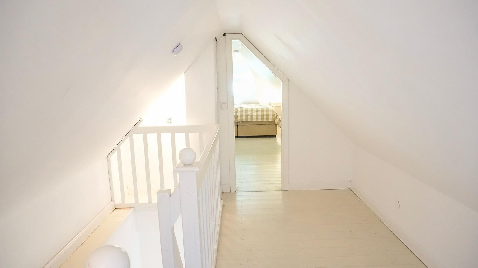 Höhlenraum mit weißen Wänden und Holzboden. Tür führt in Schlafzimmer mit Bett.