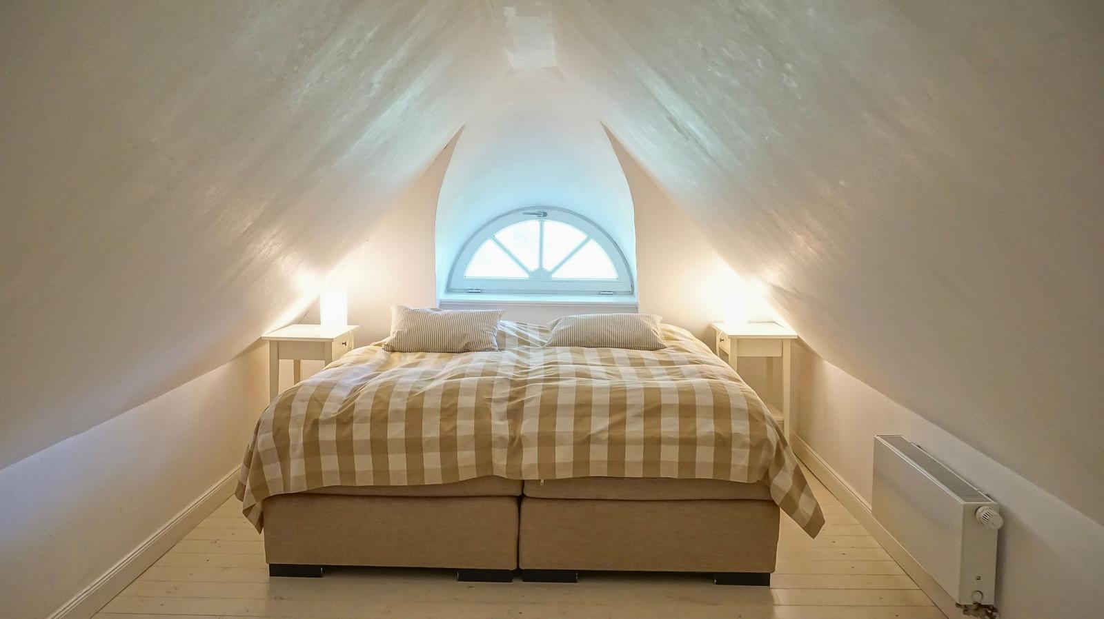 Schlafzimmer mit Dachschrägen, Bett, Nachttisch und Fenster