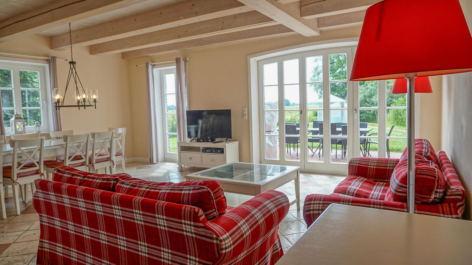 Wohn- und Essbereich mit rotem Plaid-Sofa, TV und Blick auf Terrasse.