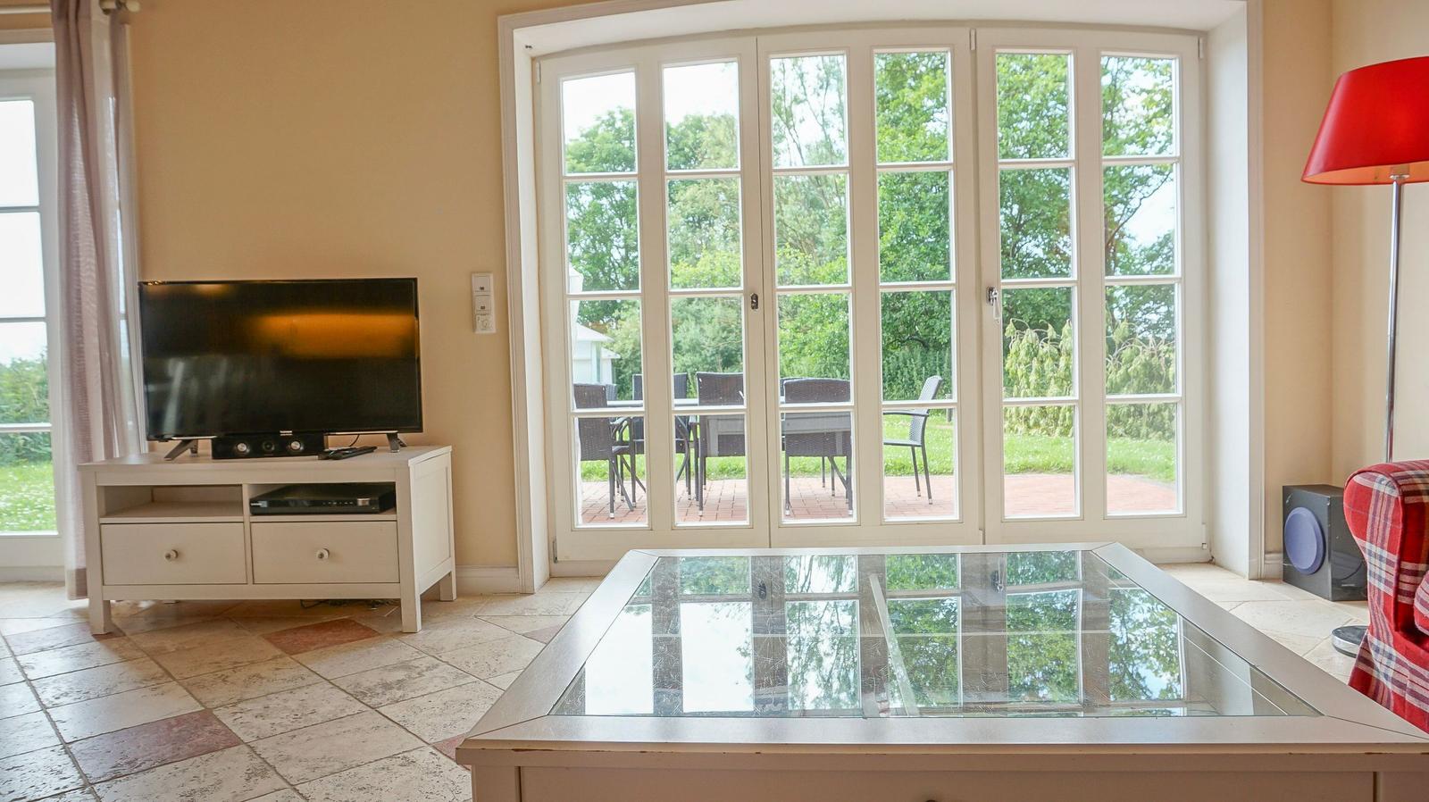 Wohnzimmer mit Glas-Tisch, TV und Blick auf den Garten.