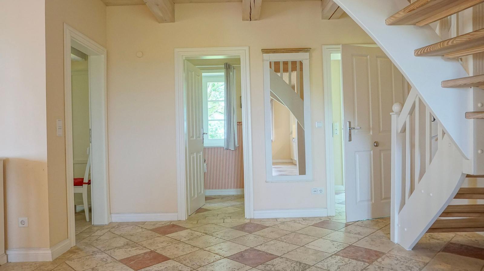 Eingangsbereich mit Fliesenboden und Holzstufen zur Treppe. Mehrere Türen führen zu weiteren Räumen.