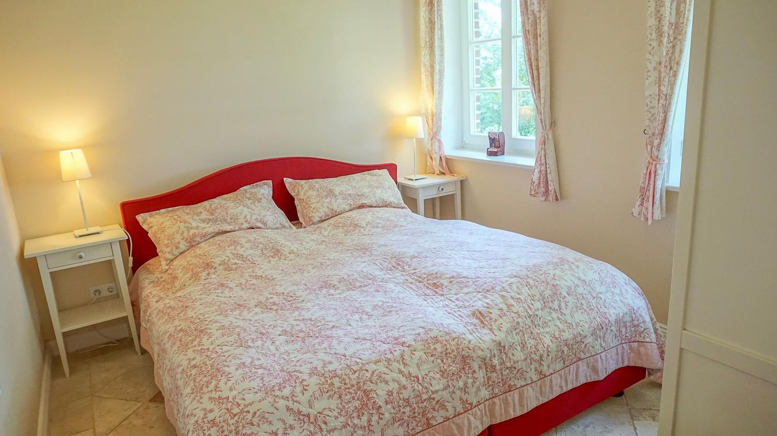 Schlafzimmer mit Bett, zwei Nachttischen und Fenster mit Vorhängen.