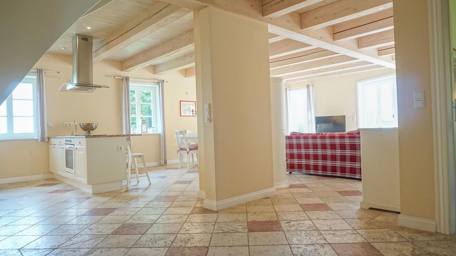 Küche mit Essbereich und Wohnzimmer mit rotem Sofa und Holzbalkendecke.