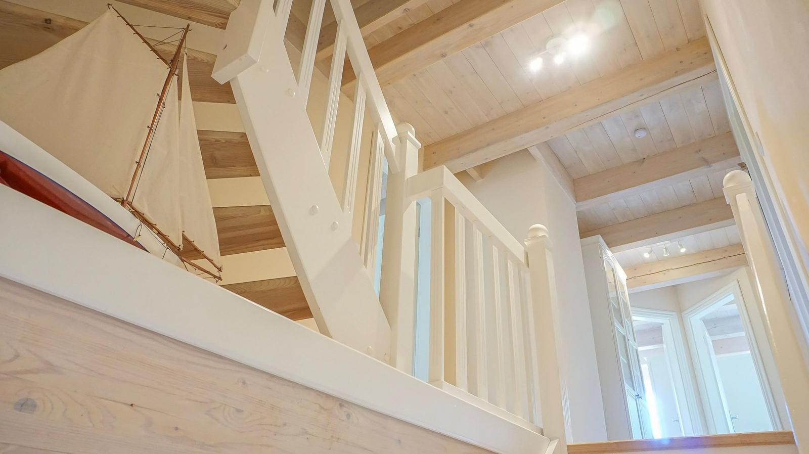 Haus mit Holzdecke, weißer Treppe und Segelschiffmodell.