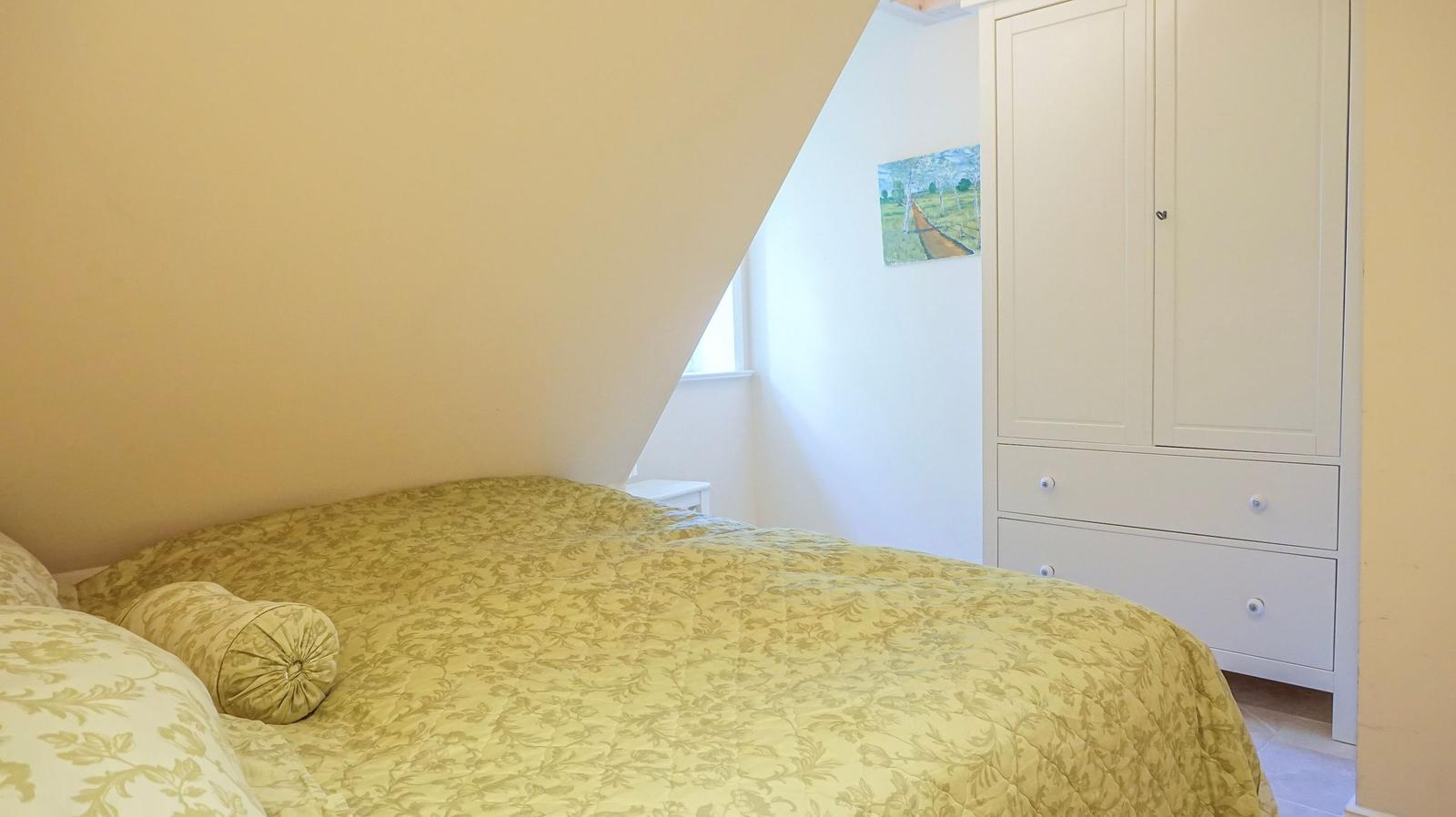 Schlafzimmer mit Bett, Kleiderschrank und Wandbild.