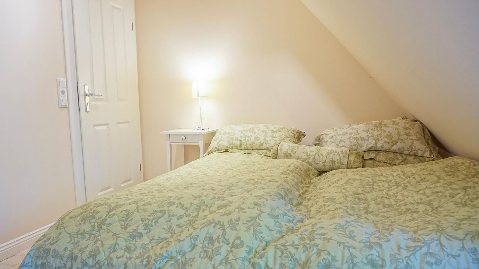 Schlafzimmer mit Doppelbett, Nachttisch und Lampe unter schräger Decke.
