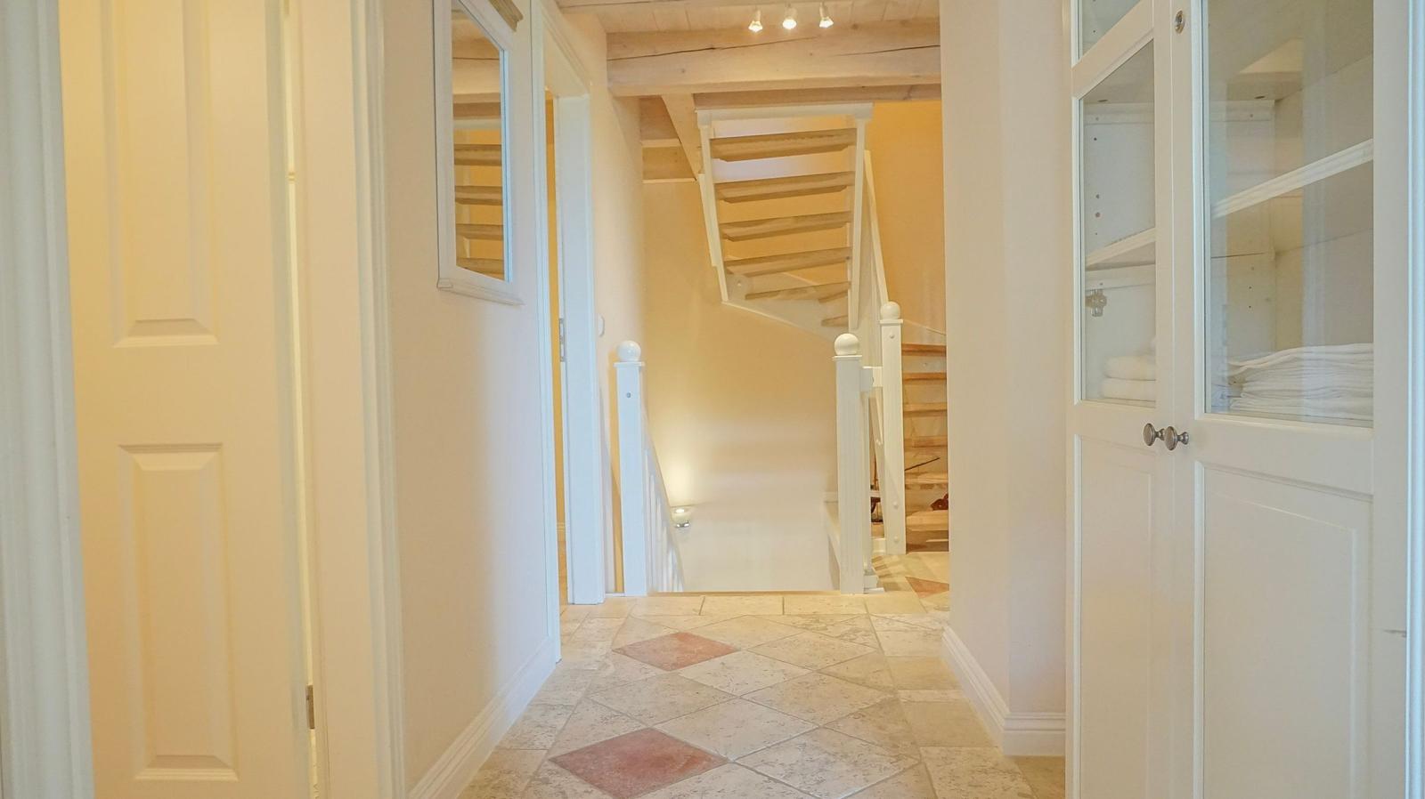 Flur mit Fliesenboden, Treppe und Schrank mit Glasfront.