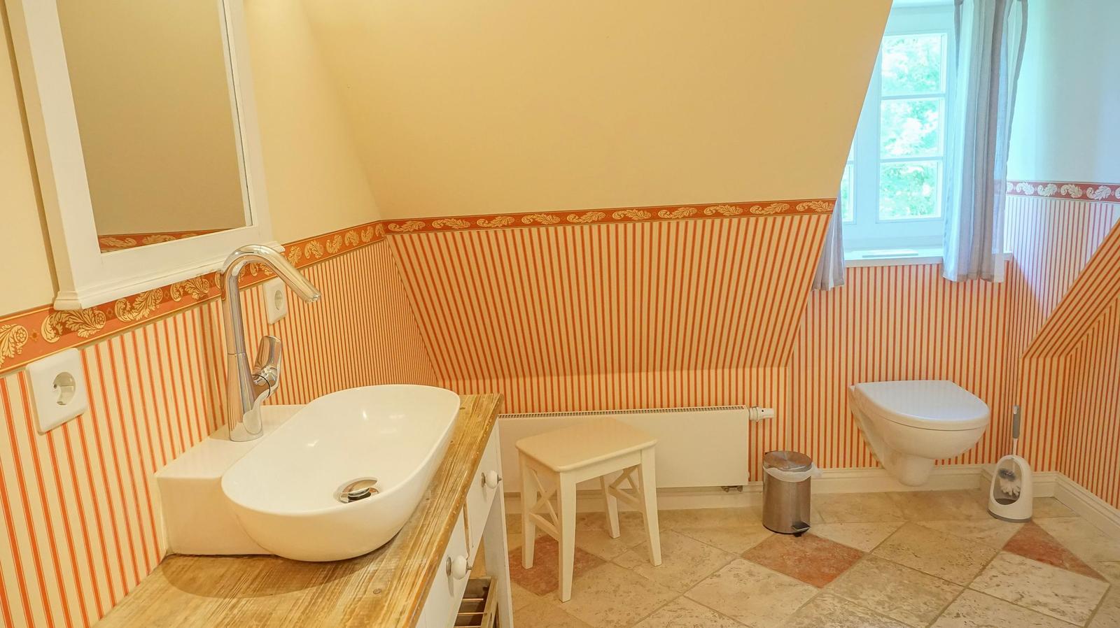 Badezimmer mit Waschbecken, Toilette und Fenster. Wandverkleidung mit Streifenmuster.