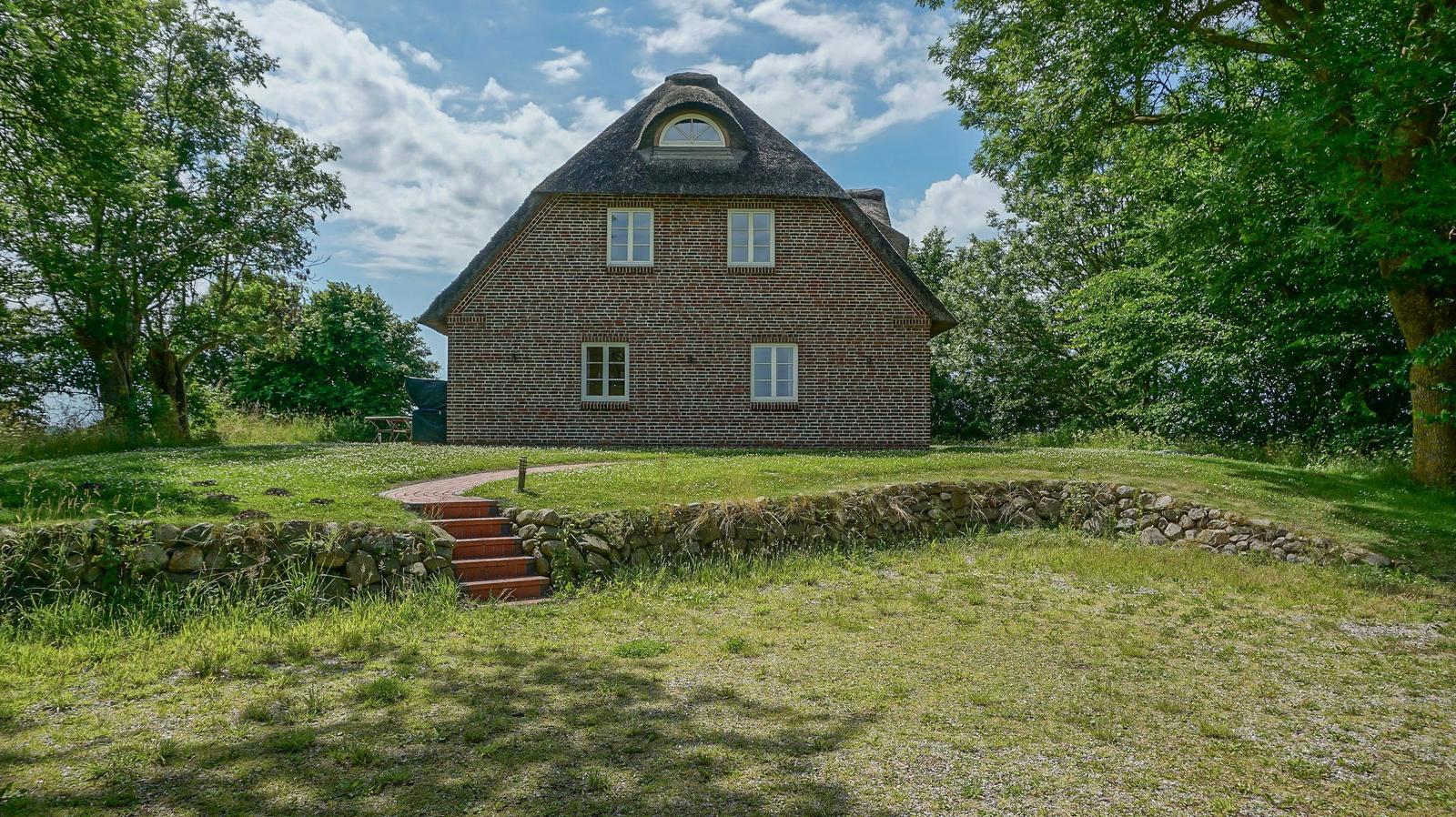Ein zweistöckiges Haus mit strohgedecktem Dach und Steinmauer im Gras.