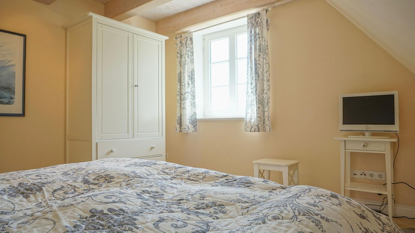 Schlafzimmer mit Bett, Kleiderschrank, Fenster und Fernseher auf Tisch