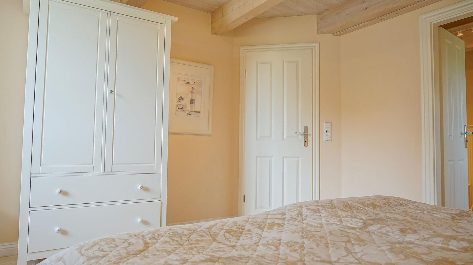 Schlafzimmer mit weißem Schrank, Bett und Holzbalken an der Decke.