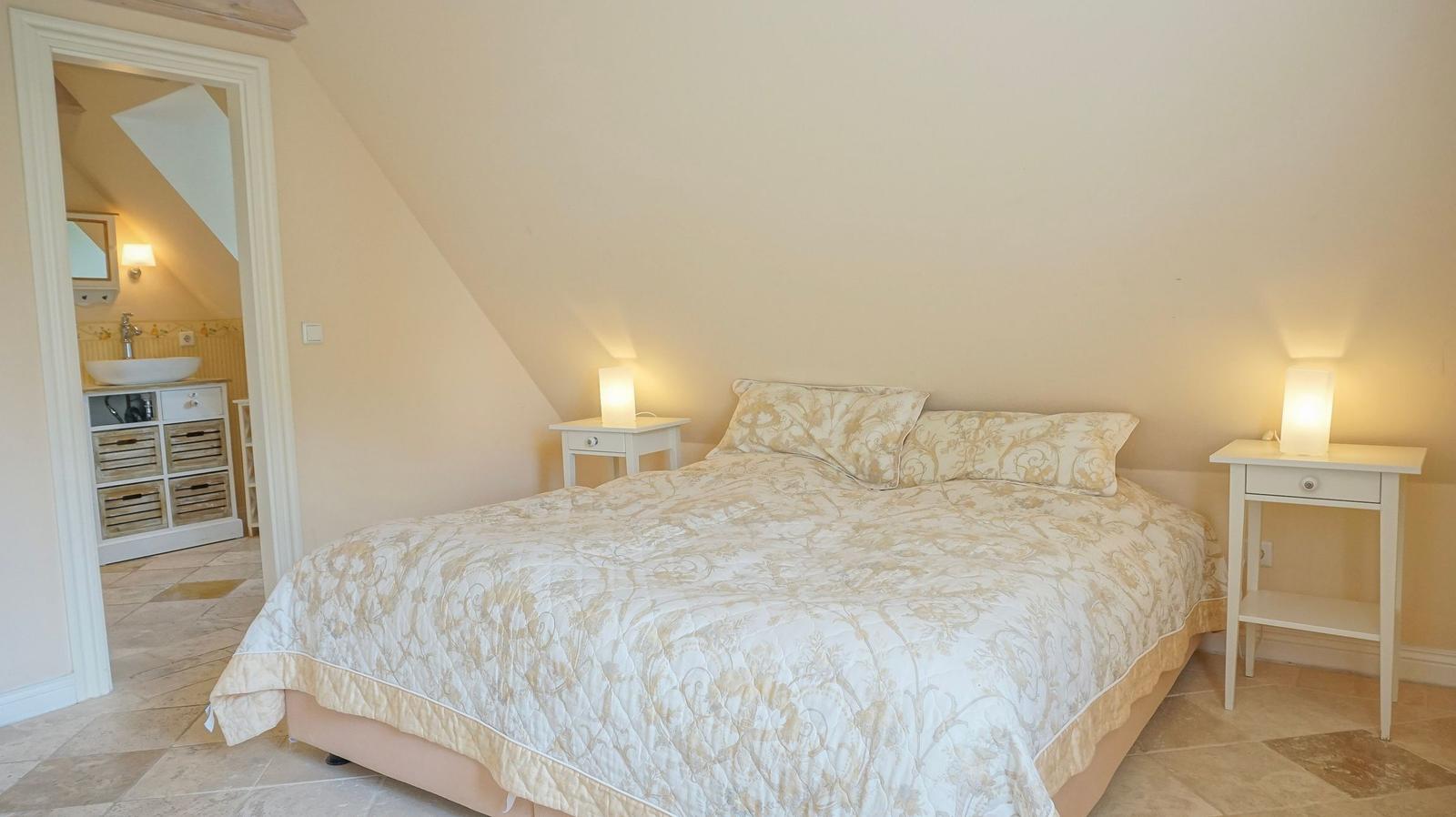 Schlafzimmer mit Doppelbett, zwei Nachttischen und angrenzender Badewanne.