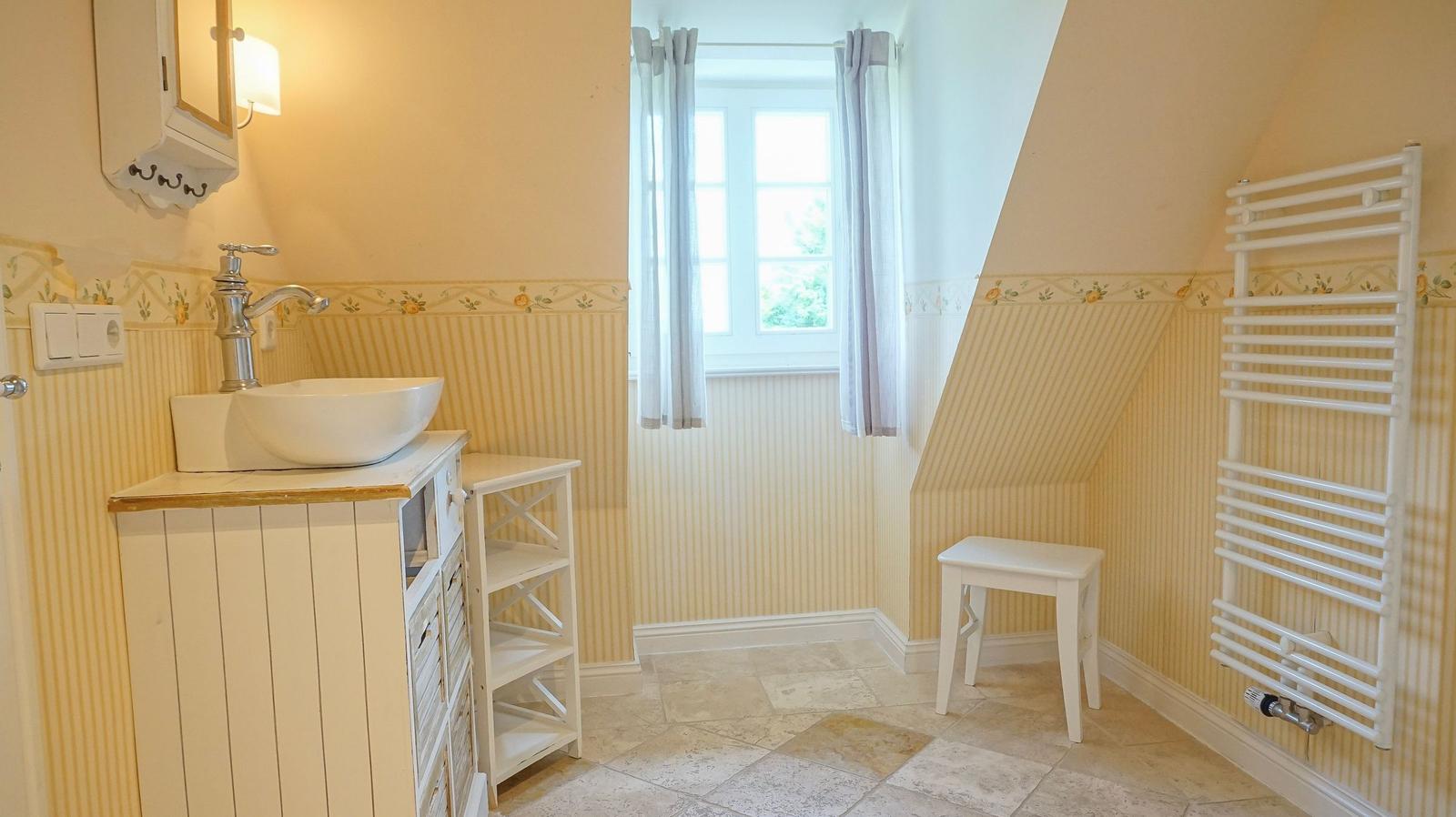 Badezimmer mit Waschbecken, Fenster, Heizkörper und Stuhl.