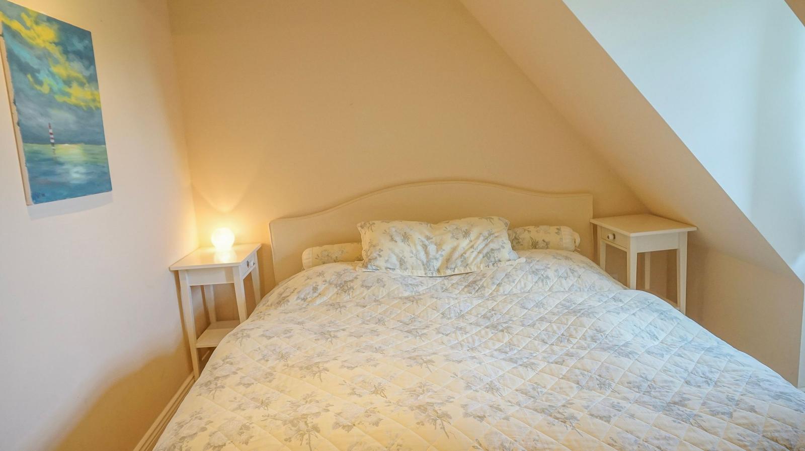 Schlafzimmer mit Bett, Nachttischen und Wandbild unter Dachschrägen.