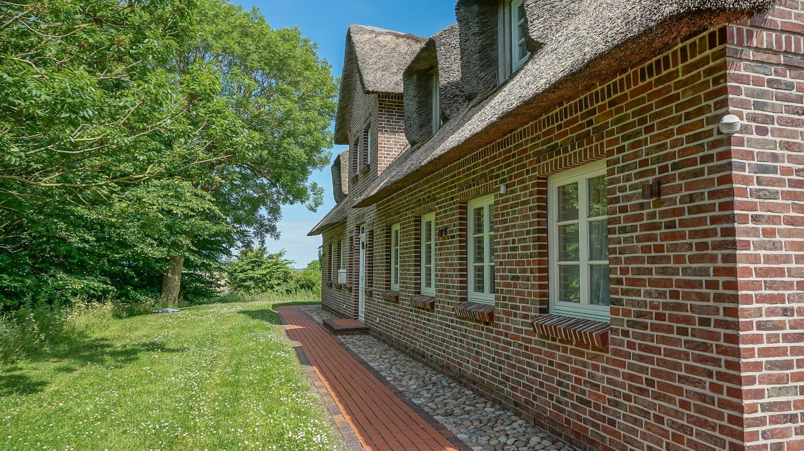 Haus mit rotem Ziegelstein und Strohdach, gepflastertes Weg und grüner Rasen.