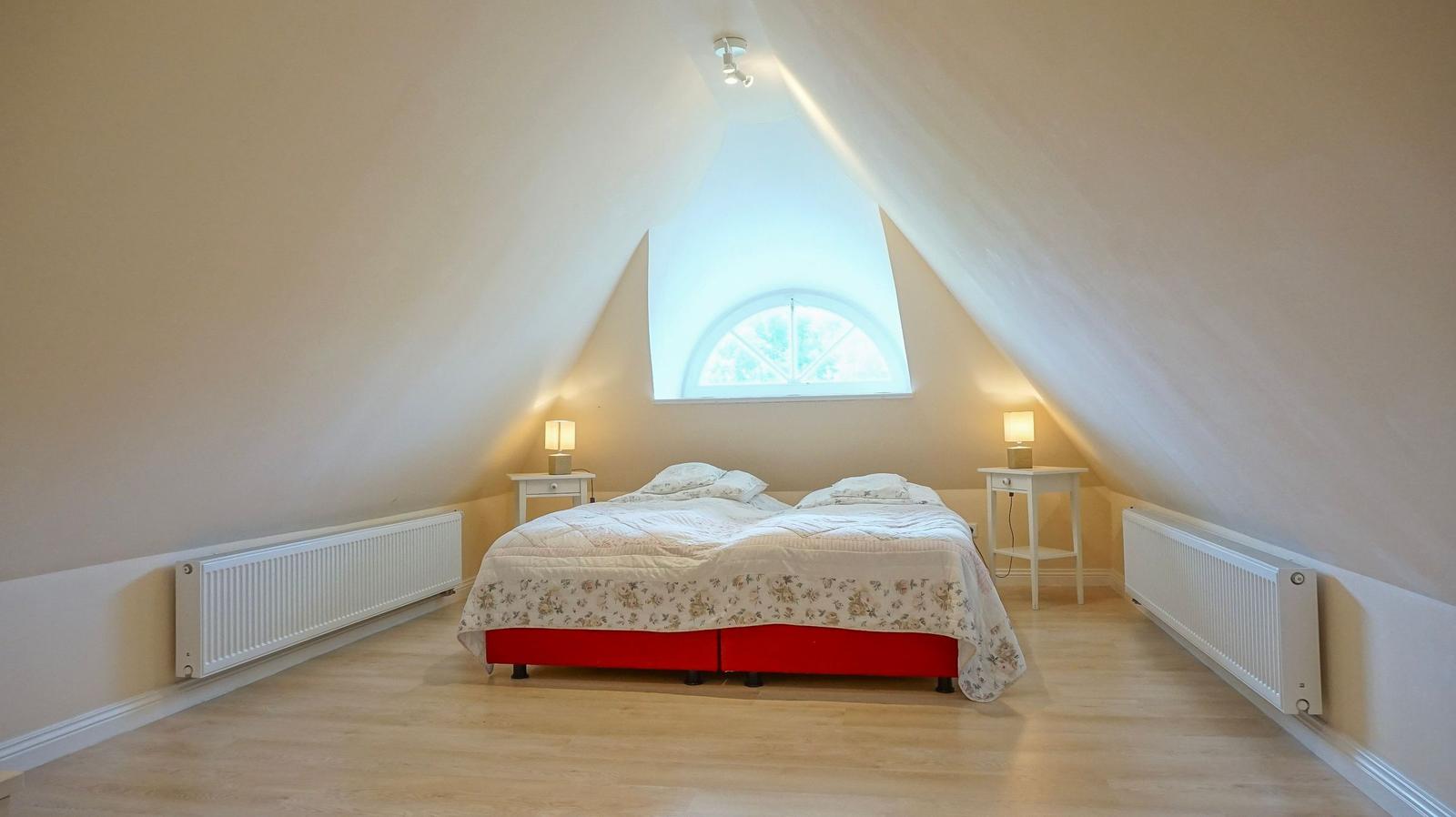 Schlafzimmer mit Dachschrägen, Bett mit floraler Bettwäsche und runden Fenstern.