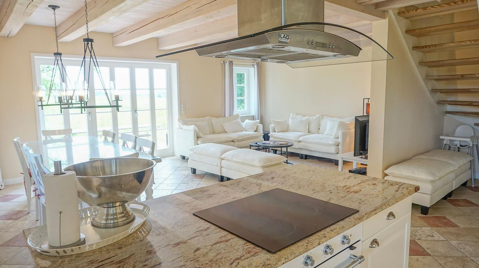 Küche mit Steinarbeitsplatte, Essbereich und Wohnzimmer mit weißen Sofas und Holzdecke.