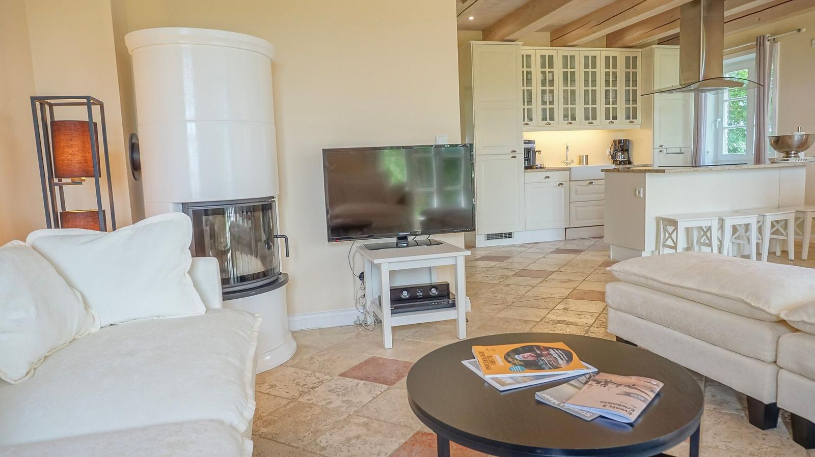 Wohnbereich mit Sofa, Kamin und TV. Küche mit Arbeitsplatte und Stühlen.
