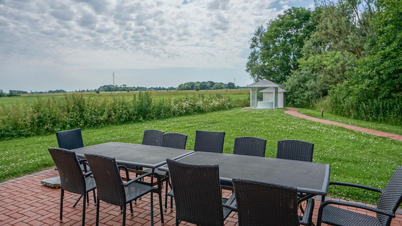 Terrasse mit Tisch und Stühlen, Blick auf Grasfläche und Pavillon.
