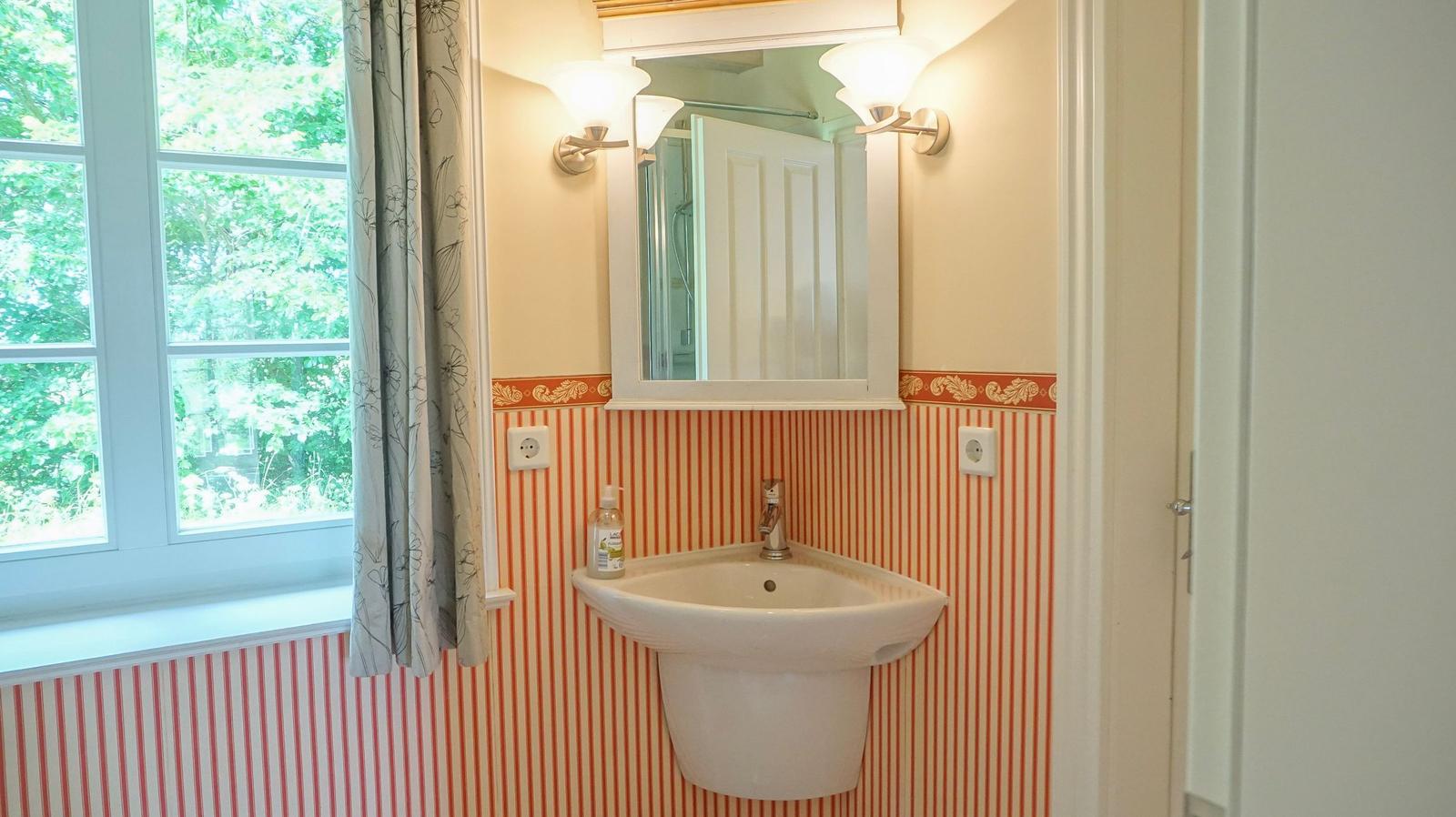 Badezimmer mit Waschbecken, Spiegel und Fenster mit Blick auf Grün.