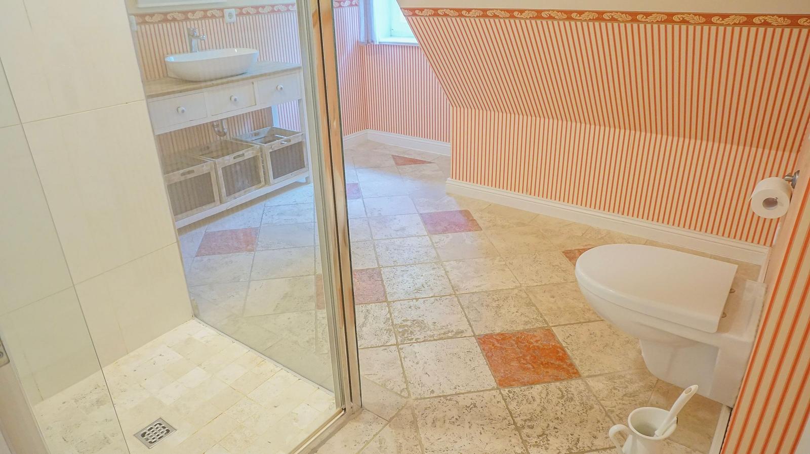 Badezimmer mit Toilette, Dusche und Waschbecken. Wandtapete mit Streifenmuster.