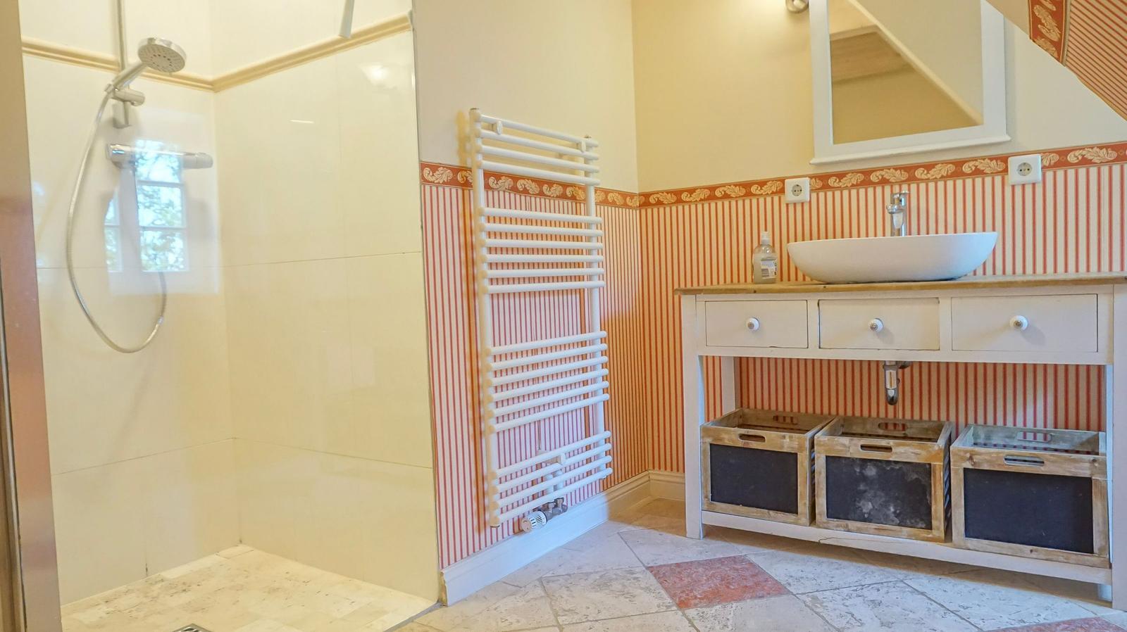 Bad mit Dusche, Waschbecken und Heizkörper an gestreifter Wand.