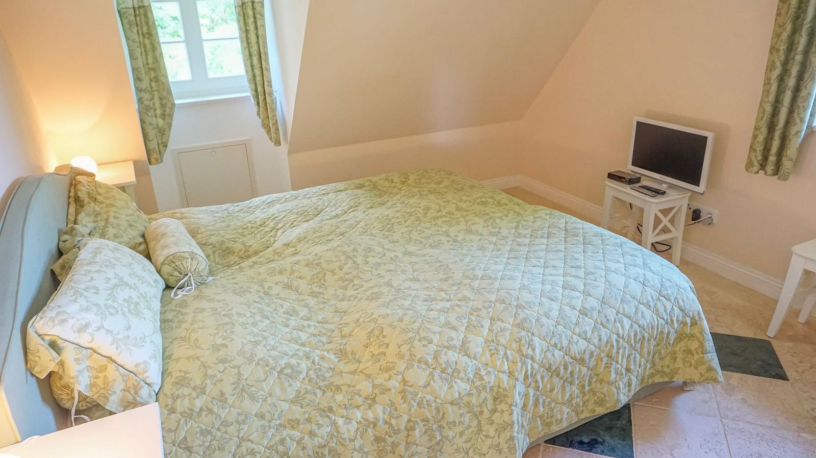 Schlafzimmer mit Bett, TV und Fenster mit Vorhängen.