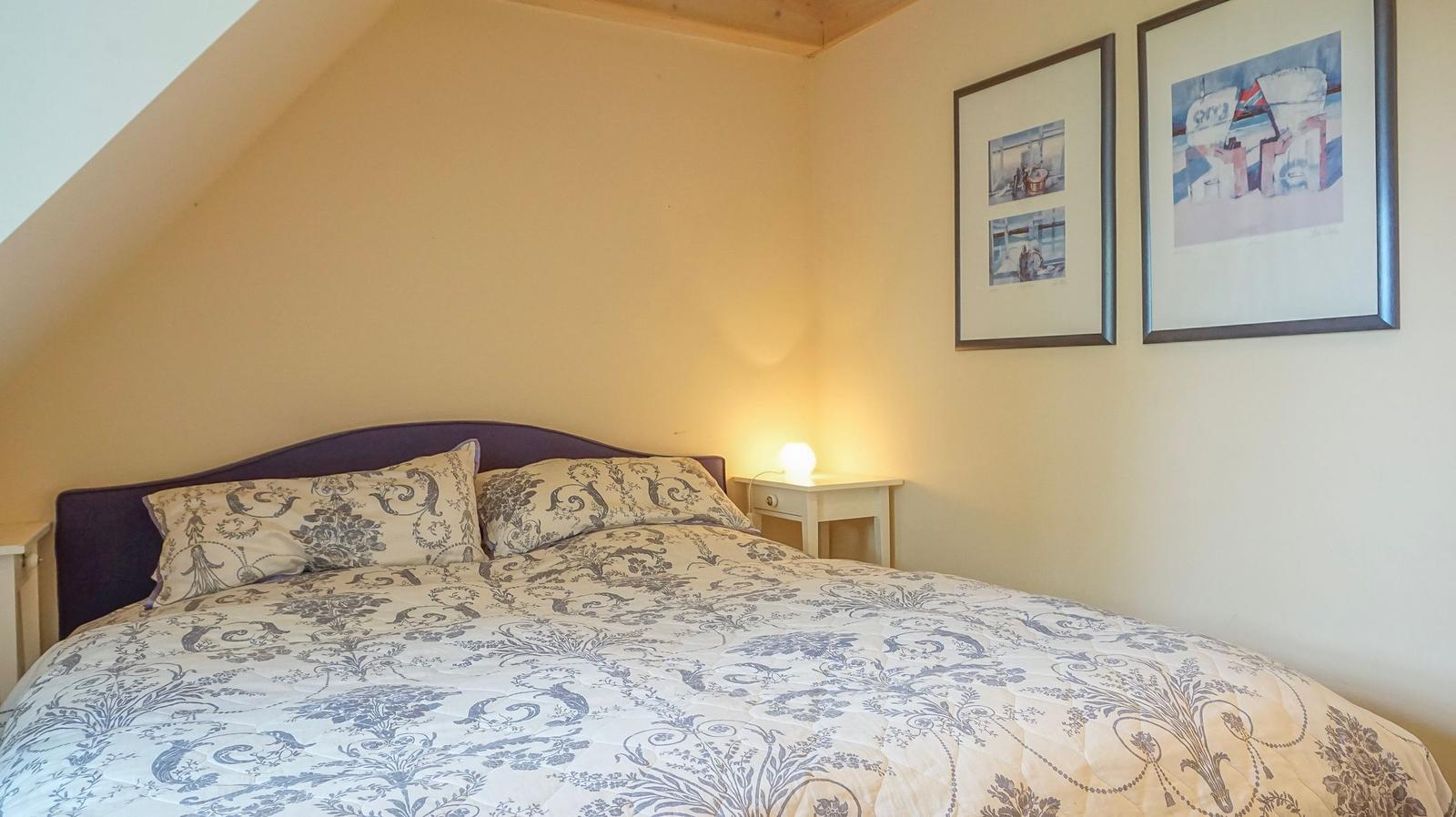 Schlafzimmer mit Doppelbett, gemütlicher Beleuchtung und zwei Bildern an der Wand.