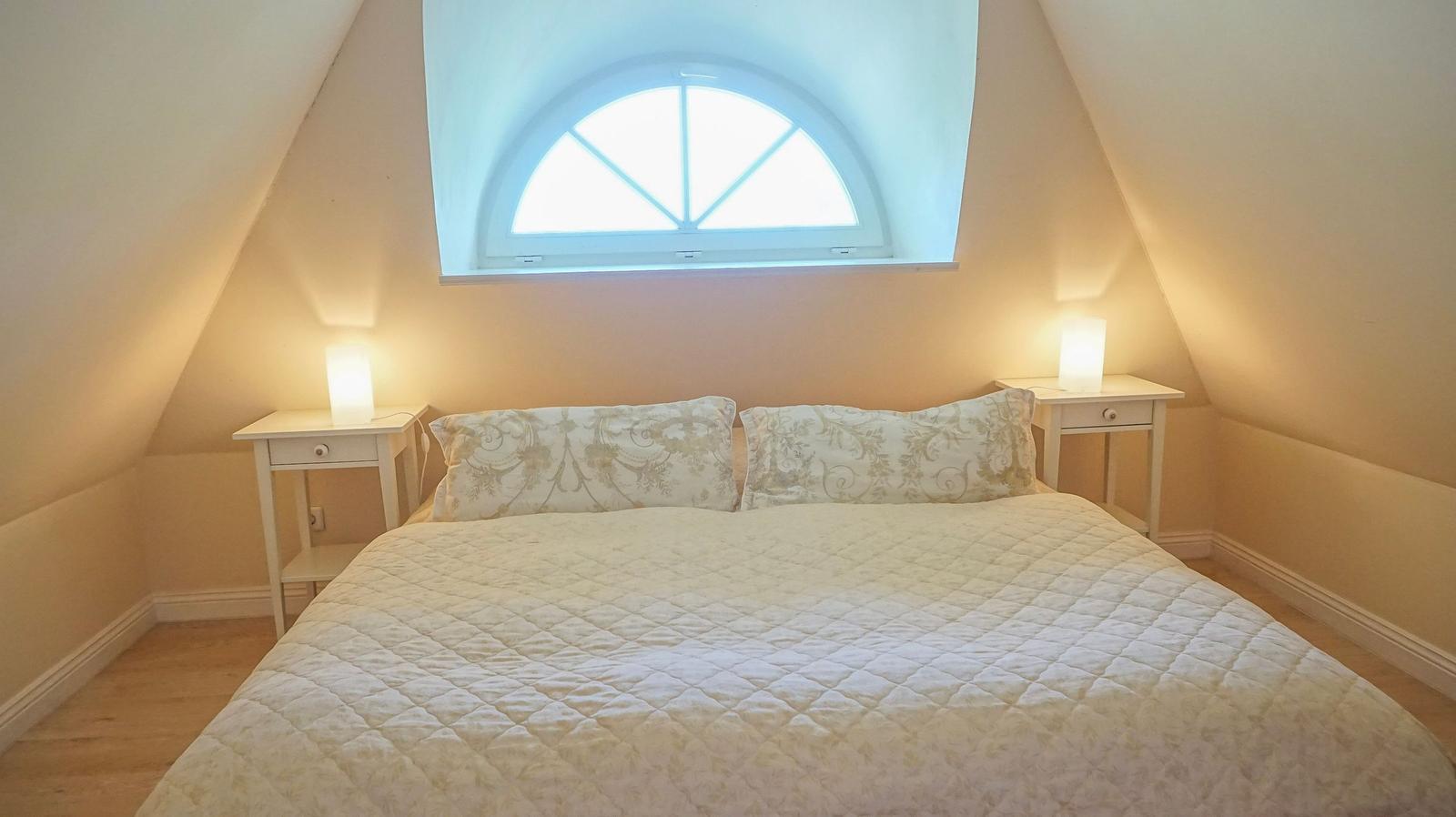 Schlafzimmer mit Dachschrägen, Bett, zwei Nachttischen und Fenster