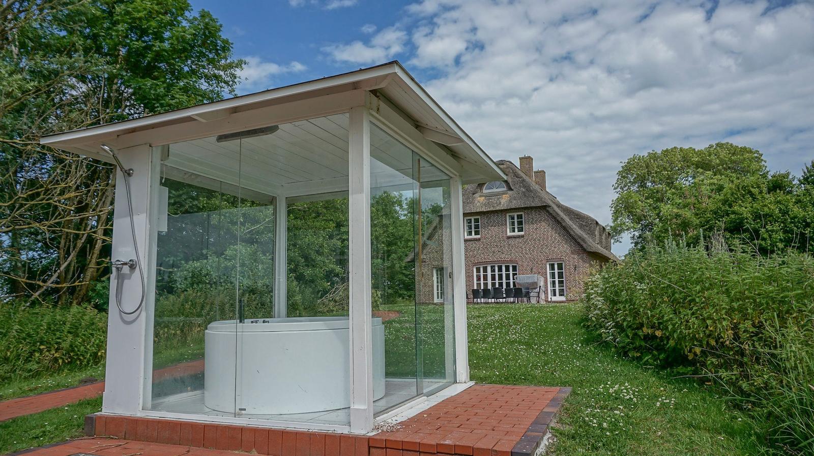 Glasstruktur mit Whirlpool und Dusche im Freien. Hintergrund: traditionelles Haus mit Schieferdach.