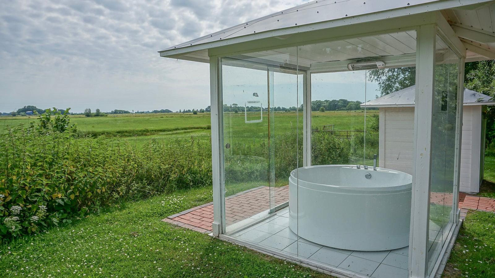 Eine runde Whirlpool-Badewanne in einer Glasveranda mit Blick auf eine grüne Landschaft.