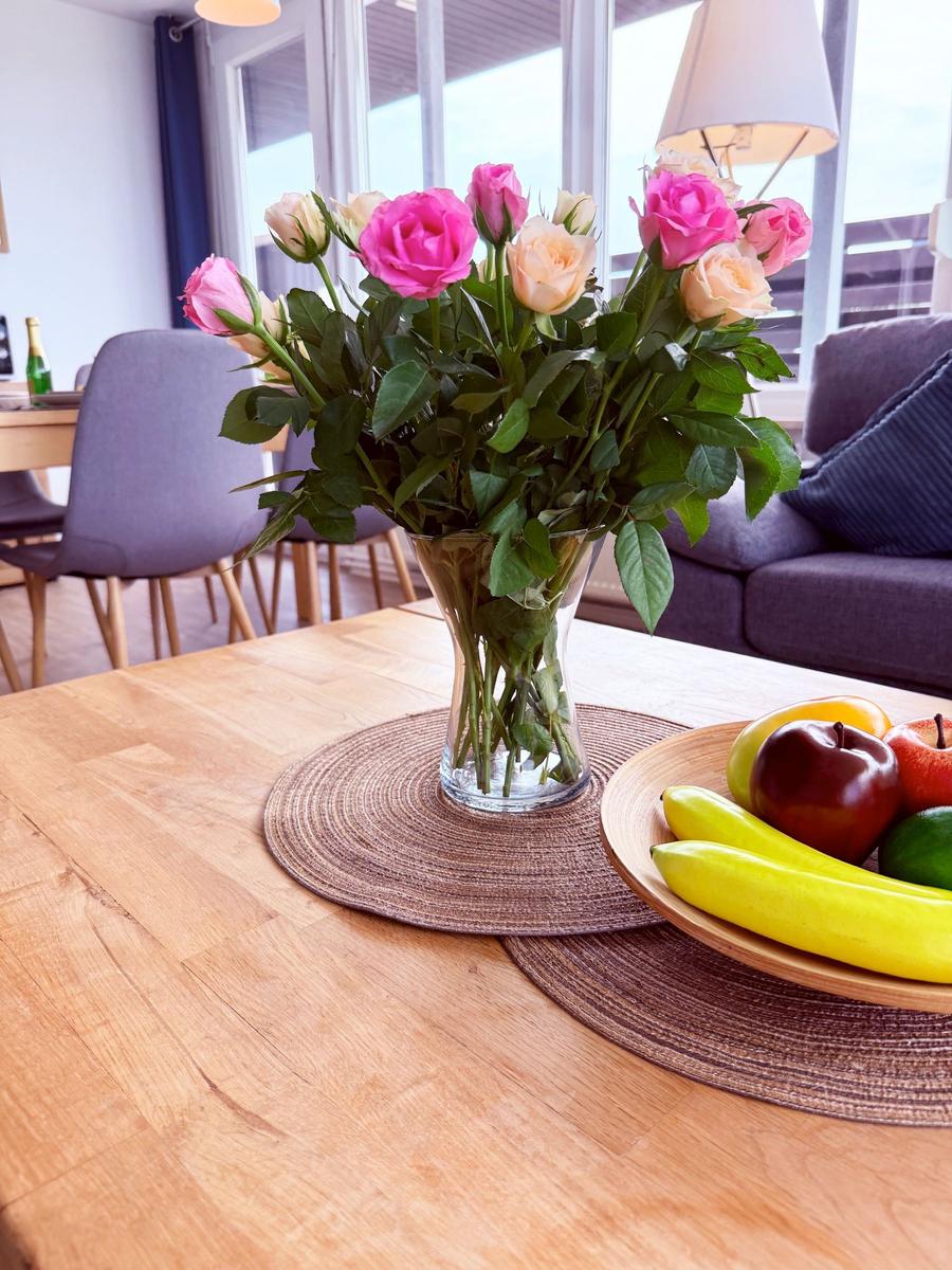 Holztisch mit Blumen und Obst, Sitzgelegenheiten im Hintergrund
