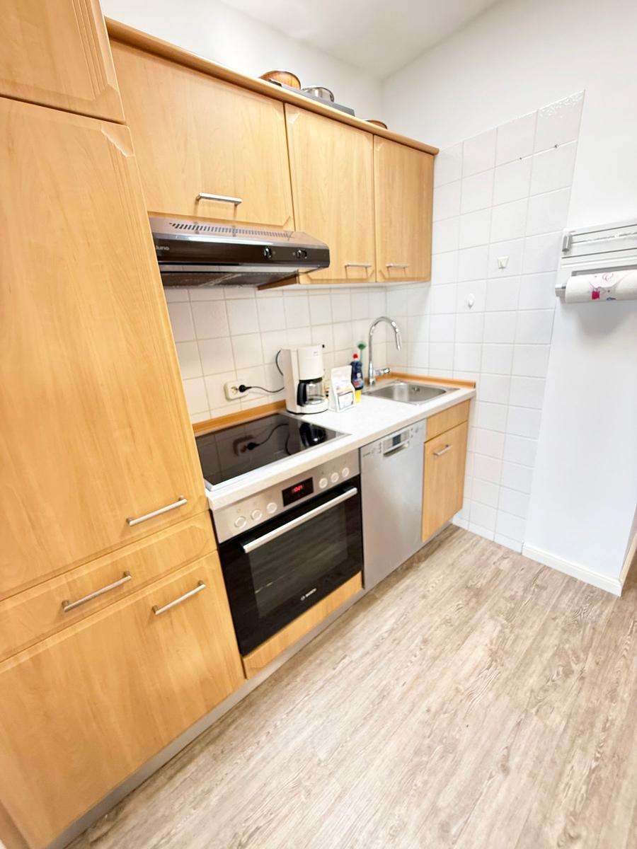 Küche mit Holzschränken, Spüle, Kühlschrank und Kochfeld.