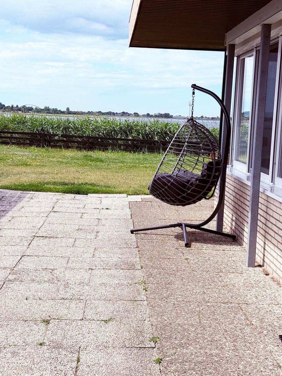 Hängesessel auf Terrasse mit Blick auf Gras und Wasser.