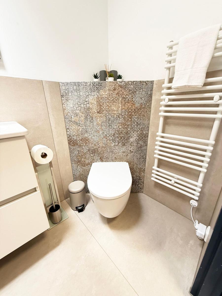 Badezimmer mit Toilette, Heizkörper und Mosaikwand