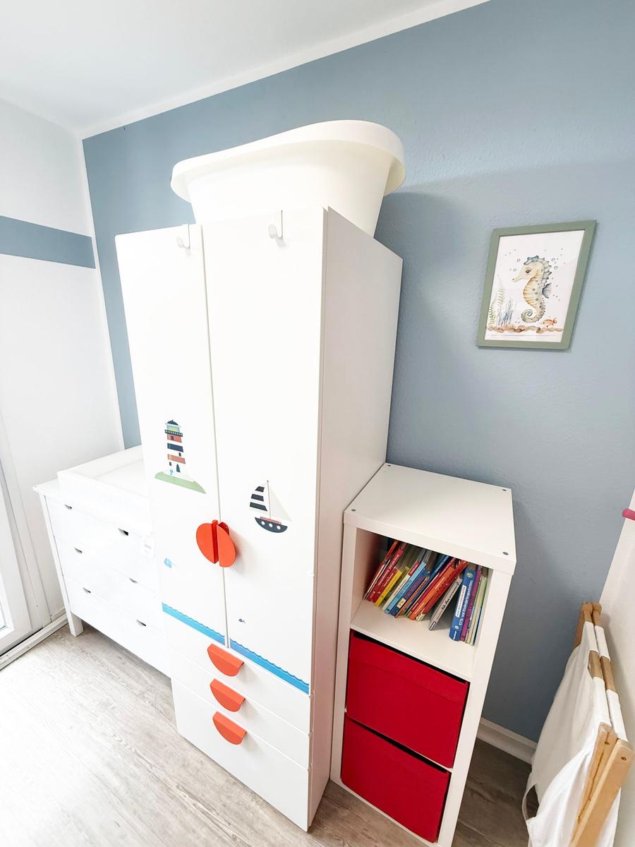 Kinderzimmer mit weißem Schrank, Bücherregal und Wandbild mit Seeoste.
