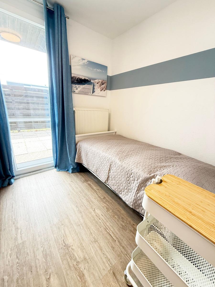 Ein Schlafzimmer mit Bett, blauen Vorhängen und Holzboden. An der Wand hängt ein Bild.